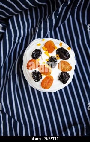 Un gâteau de Pâques décoré d'abricots et de pruneaux séchés se dresse sur un tablier rayé bleu. Concept de vacances religieuses de Pâques, vue de dessus. Banque D'Images