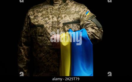 Un soldat des forces armées ukrainiennes est accompagné d'un drapeau bleu-jaune de l'Ukraine sur fond noir. Honorer les anciens combattants et commémorer les morts dans la guerre Banque D'Images