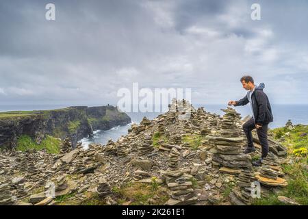 Homme gerbage en pierre dans les falaises emblématiques de Moher, en Irlande Banque D'Images