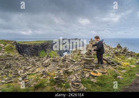 Homme gerbage en pierre dans les falaises emblématiques de Moher, en Irlande Banque D'Images