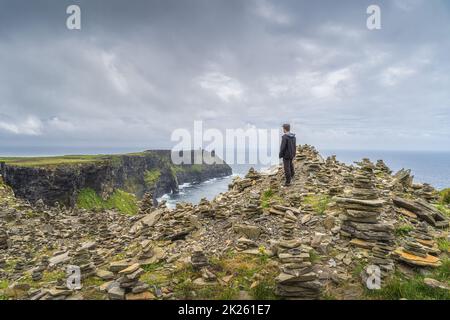 Homme debout entre des pierres et admirant la vue sur les falaises emblématiques de Moher, en Irlande Banque D'Images