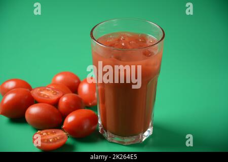 Plein verre de jus de tomate frais avec tomates cerises autour.Jus de tomate très savoureux et sain avec des glaçons Banque D'Images