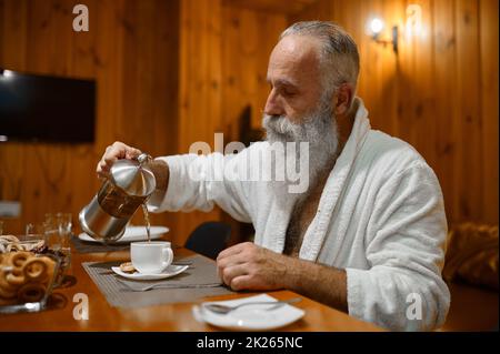 Homme versant du thé pendant le repos dans le sauna Banque D'Images