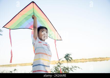 Un petit garçon asiatique heureux avec un cerf-volant qui s'évolera dans le parc Banque D'Images