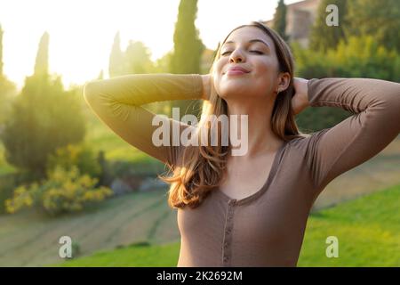 Portrait d'une femme libre respirant de l'air frais dans la nature. Bonne fille avec les mains derrière sa tête en bonheur. Détente, calme extérieur, bien-être concept sain de style de vie. Banque D'Images