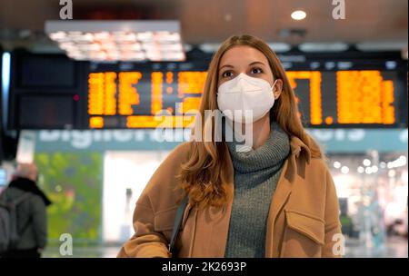 Femme d'affaires portant un masque facial FFP2 KN95 à la gare et gardant la distance sociale. Jeune femme attendant le train avec des horaires sur fond. Banque D'Images