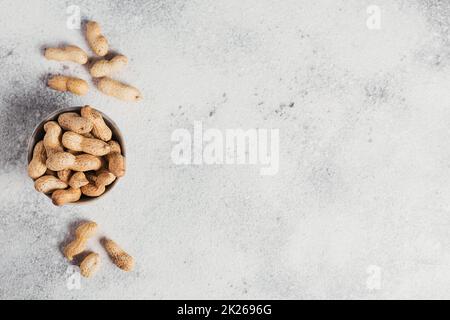 Pile de arachides dans un bol sur fond blanc. Des noix fraîches dans leurs coquilles. Banque D'Images