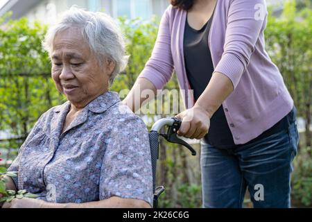 Le soignant aide la femme asiatique âgée ou âgée en fauteuil roulant dans le parc. Banque D'Images