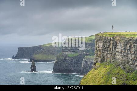 Des oiseaux de mer survolant les falaises emblématiques de Moher avec la tour OBriens sur une longue distance, en Irlande Banque D'Images