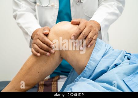 Médecin asiatique physiothérapeute examinant, massant et traitement genou et jambe d'un patient senior dans la clinique orthopédique infirmière hôpital. Banque D'Images