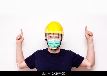 Travailleur d'interprétation derrière un fond blanc. Port d'un masque vert et d'un casque jaune Banque D'Images