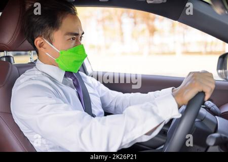Homme d'affaires portant un masque médical de protection et conduisant dans la voiture pendant l'épidémie de coronavirus Banque D'Images