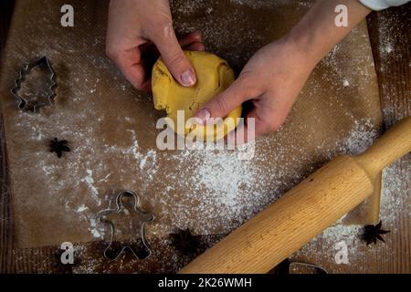 Au premier plan se trouve une table avec du parchemin de cuisson, sur laquelle il y a de la pâte que les mains du cuisinier sont en train de s'émietter, une broche de roulades, des moules de cuisson et de la farine sont éparpillés. Banque D'Images