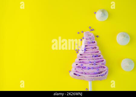 Sapin de Noël violet pâle en meringue sur bâton, décoré de boules pourpres et argentées sur fond jaune vif, de boules de poudre pourpres et de perdrix blancs sont dispersés près de l'arbre. Banque D'Images