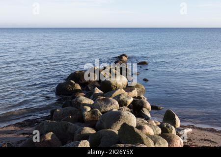 Groyne fait de rochers sur la côte de la mer Baltique devant un horizon lointain Banque D'Images