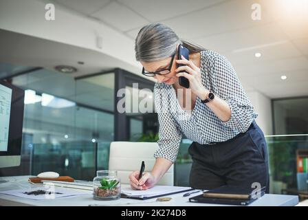 Les rendez-vous sont en cours de remplissage.Photo d'un psychologue convaincu et mature utilisant un smartphone et prenant des notes dans un bureau moderne. Banque D'Images