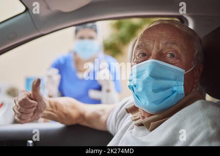 Restez en sécurité et faites-vous vacciner.Photo d'un homme âgé et d'un jeune professionnel de la santé montrant un pouce vers le haut à un trajet à travers le site de vaccination. Banque D'Images