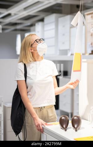 Nouvelle normale pendant l'épidémie de covid. Femme caucasienne magasiner au magasin de meubles et d'accessoires à la maison portant un masque médical de protection pour prévenir la propagation du virus corona Banque D'Images
