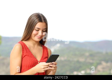 Joyeux adolescent dans rouge vérifier téléphone à l'extérieur Banque D'Images