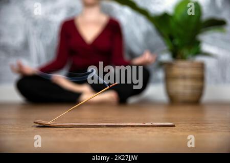 Femme consciente méditant à la maison avec des bâtons d'encens brûlants, se sitant dans la pose de lotus. Tenir les mains sur les genoux avec les paumes orientées vers le haut. Banque D'Images