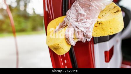 Jeune femme nettoyant une partie de la porte de voiture, détail de gros plan à la main dans un gant tenant une éponge jaune Banque D'Images