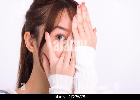 Jeune femme couvrant le visage avec les mains et piquant à travers ses doigts à la caméra Banque D'Images