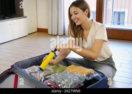 Belle femme souriante utilisant une pompe à vide permettant d'économiser de l'espace dans ses bagages assis sur le sol.Passer l'aspirateur dans l'emballage comprimé pour le stockage des vêtements. Banque D'Images