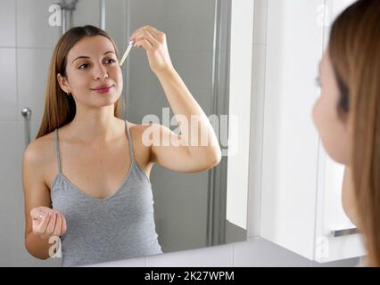 Soin de la peau pour jeunes. Belle fille appliquant un rappel de vitamine C antioxydant acide ascorbique anti sérum de vieillissement sur son visage tout en tenant une pipette dans sa main. Banque D'Images