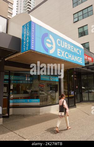 Jeune femme élégamment habillée qui passe devant l'enseigne du guichet du change international sur la rue Robson, au centre-ville de Vancouver, en Colombie-Britannique, au Canada Banque D'Images