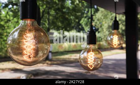 Les ampoules à incandescence Edison sont suspendues dans un style loft rétro. Décoration de la cafétéria en gros plan. Décoration de rue, lanternes claires, lumière chaleureuse. Mise au point douce, arrière-plan de rue flou Banque D'Images