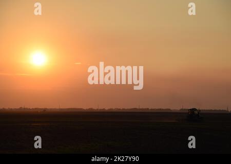 Le tracteur labourage le champ sur un coucher de soleil de fond. silhouette du tracteur sur fond de coucher de soleil Banque D'Images