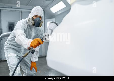 Technicien en vêtements de sécurité pulvérisant de la peinture pour voiture Banque D'Images