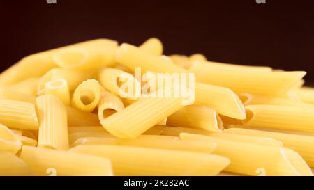 Les pâtes brutes Penne Rigate sont des pâtes courtes à découpes obliques et à surface nervurée. Pâtes italiennes traditionnelles. Fond de pâtes. Vue latérale sur les ingrédients italiens. Banque D'Images