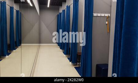 Intérieur boutique, cabine d'essayage dans un centre commercial. Personne. Les cabines d'essayage vides sont dotées de rideaux bleus et de murs gris et d'un grand miroir. Vestiaires dans un magasin de vêtements sans personnes. Banque D'Images