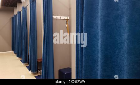 Intérieur boutique, cabine d'essayage dans un centre commercial. Personne. Les cabines d'essayage vides sont dotées de rideaux bleus et de murs gris et d'un grand miroir. Vestiaires dans un magasin de vêtements sans personnes. Banque D'Images