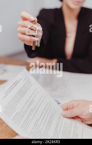 Jeune femme Realtor tient les clés de l'immobilier, le client lit le contrat. Location et achat de biens immobiliers Banque D'Images