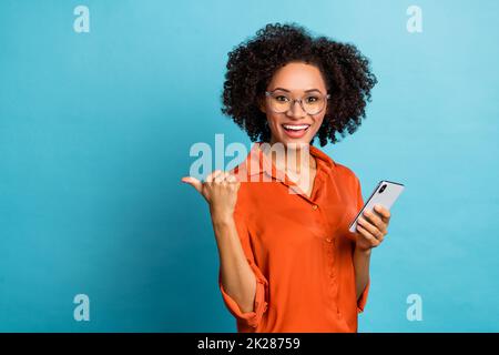 Portrait of attractive trendy cheery wavy-haired girl using gadget showing copy space smm ad isolated over bright blue color background Stock Photo