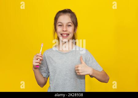 Belle adolescente aux cheveux bruns se tenant se brossant les dents avec une brosse à dents sur fond jaune, concept de nutrition et d'hygiène bucco-dentaire pour les enfants Banque D'Images