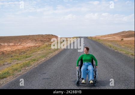 Woman in a wheelchair on a highway in the steppes.  Stock Photo