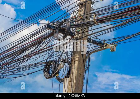 Chaos absolu de câble sur le mât de puissance thaïlandais bleu ciel de Thaïlande. Banque D'Images