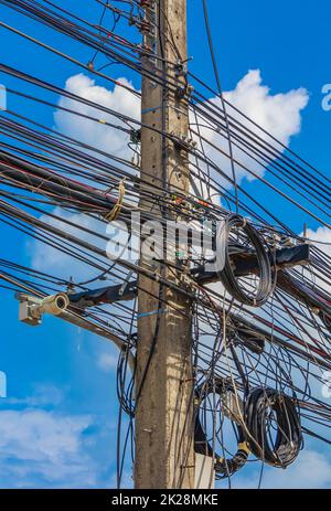 Chaos absolu de câble sur le mât de puissance thaïlandais bleu ciel de Thaïlande. Banque D'Images