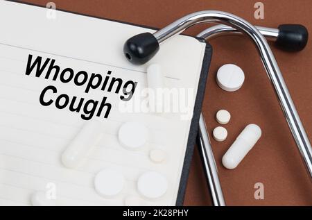 Medical concept. On a brown surface lies a stethoscope, pills and a notepad with the inscription - Whooping Cough Stock Photo