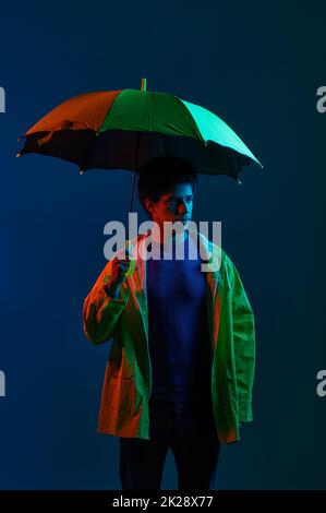 Homme en imperméable sous parapluie sur fond sombre de studio Banque D'Images