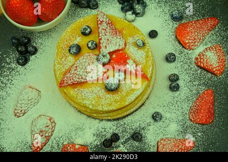 Crêpes aux baies de fruits sur fond noir.Crêpes fraîches.Bleuets, fraises et sucre glace sur crêpes.Pose à plat Banque D'Images