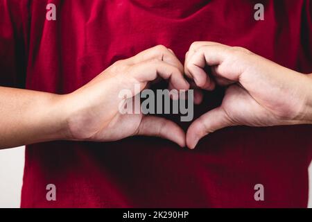 La personne montre des mains signe d'amour près de la poitrine. L'homme avec une chemise rouge en gros plan moyen. Banque D'Images