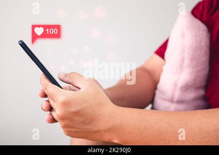 Concept de la Saint-Valentin. L'homme utilise le signe de la main pour donner et recevoir l'amour à travers un smartphone. Effet visuel en forme de coeur. Vue latérale. Banque D'Images