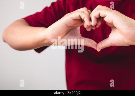 La personne montre des mains signe d'amour près de la poitrine. L'homme avec une chemise rouge en gros plan moyen. Concept de la Saint-Valentin. Espace de copie pour les messages, les mots et les textes. Banque D'Images