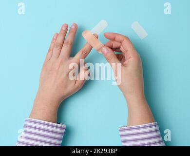 pansement médical adhésif marron et main femelle pour le traitement des blessures et des coupures sur la peau, fond bleu Banque D'Images