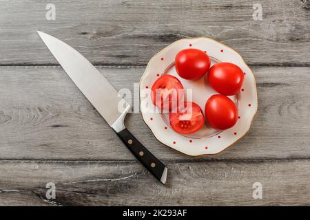 Les tomates, l'un d'entre eux réduit de moitié sur l'assiette de porcelaine blanche avec de petits points rouges, couteau chef situées près de. Vue sur table. Banque D'Images