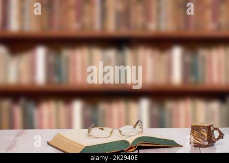 Livres arrière-plans. Gros plan d'un livre ancien avec des lunettes de lecture et une tasse d'argile brune sur un bureau rose clair au-dessus d'une étagère floue dans la bibliothèque. Concept d'éducation. Journée des enseignants. Banque D'Images